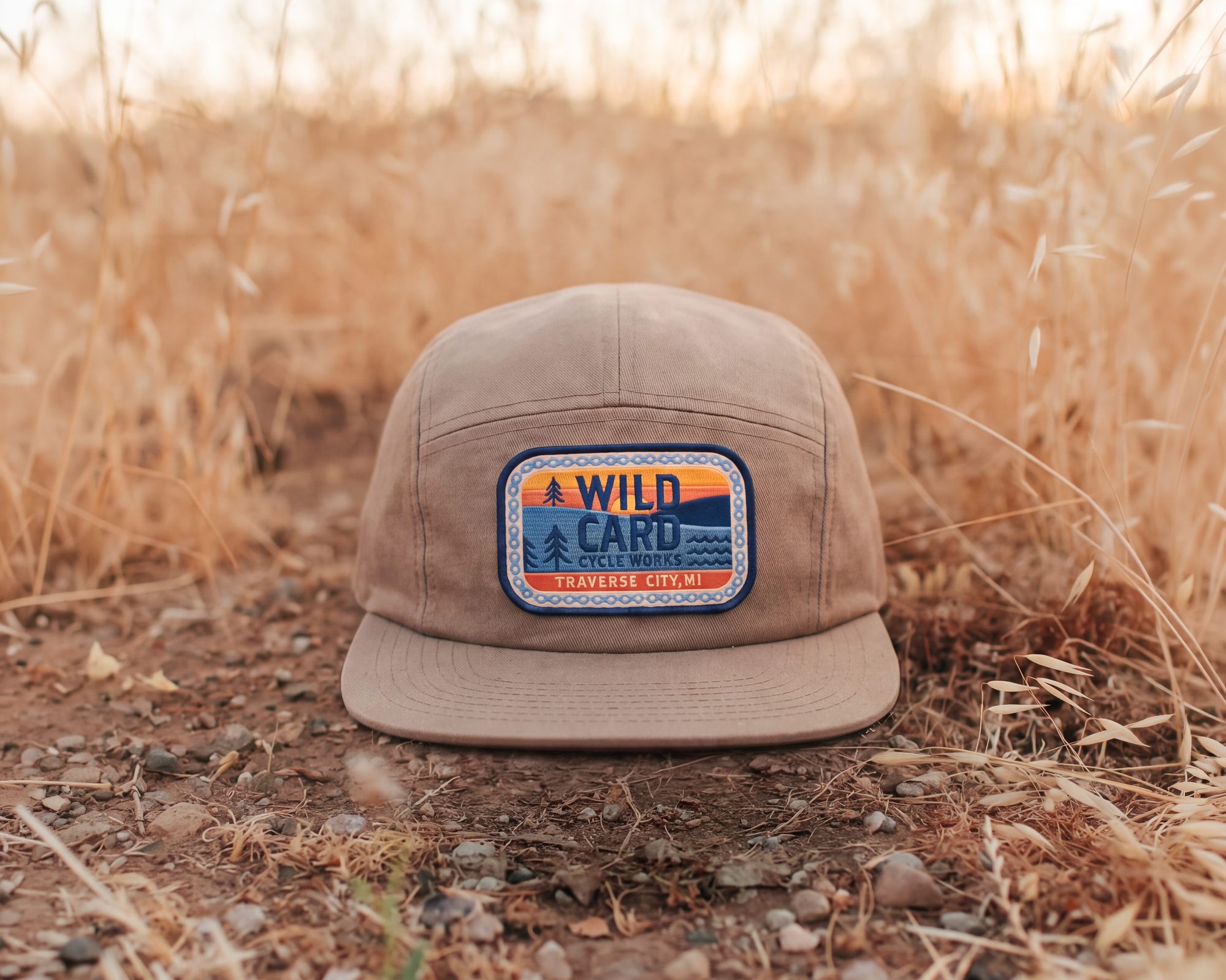 A tan hat wearing the Wild Card Cycle Works patch, resting in dry grass