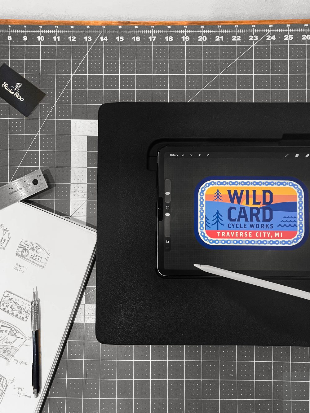 The finished patch artwork on an iPad on a cutting mat, beside a sketchbook of patch thumbnails